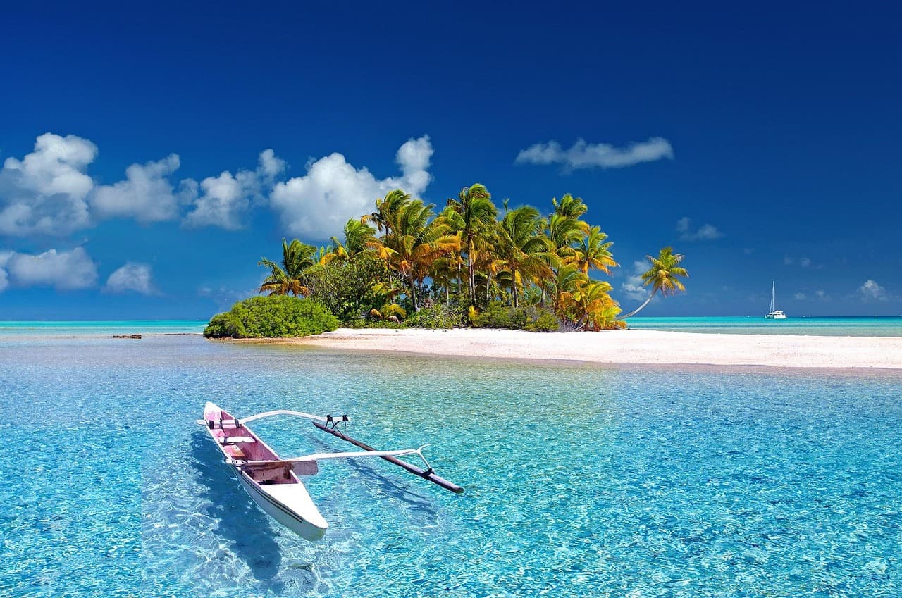 Pirogue à balancier sur un lagon turquoise devant un motu bordé de palmiers