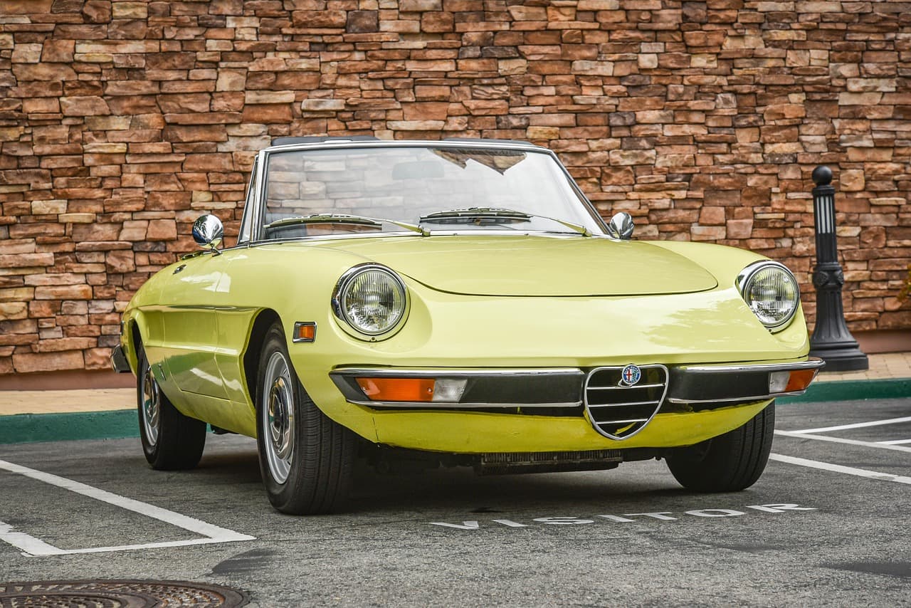 Cabriolet ancien jaune stationné devant un mur de pierres
